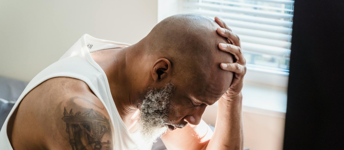 A man is looking down and holding his head while thinking about inhalant abuse.