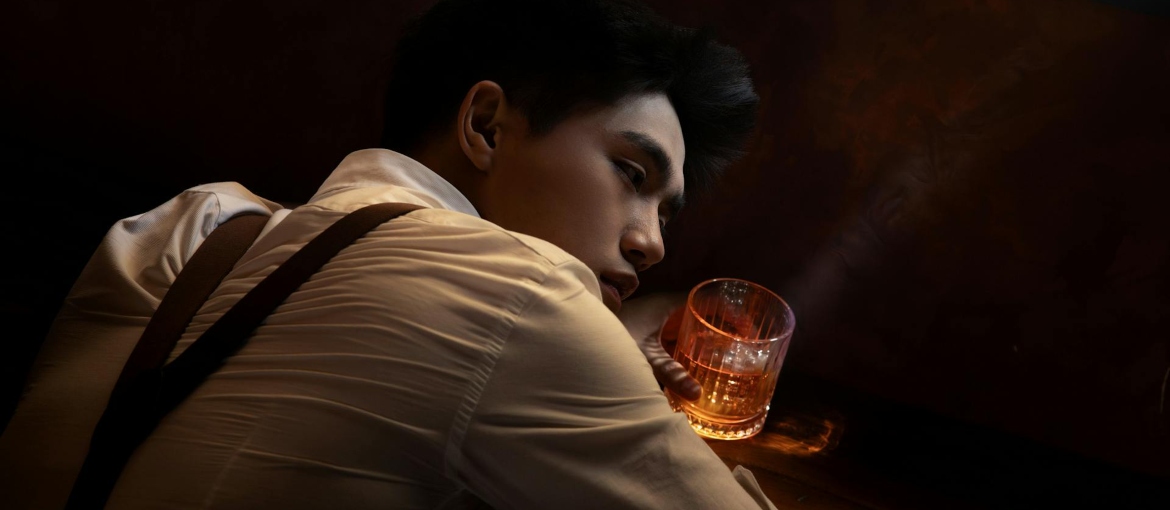 A drunk man is lying on the black surface, and holding a glass of alcohol.