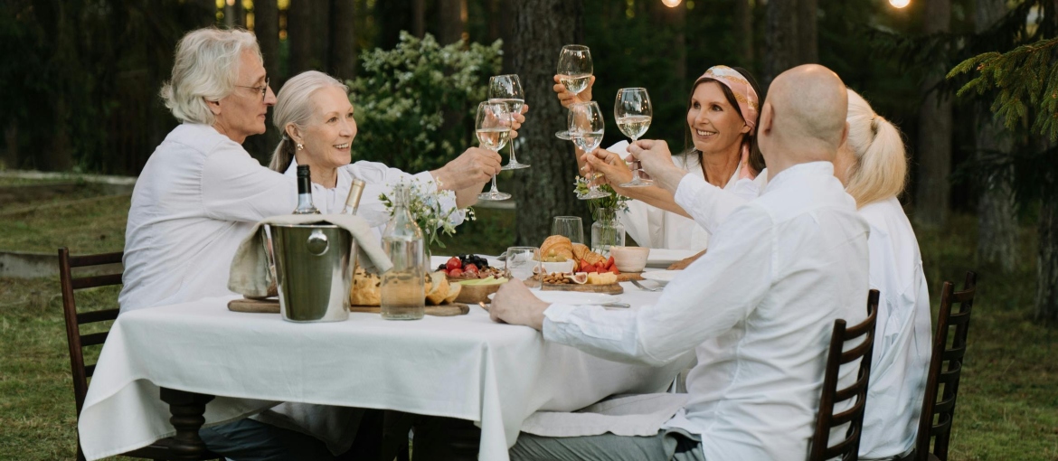 Family sitting at a table in the yard eating lunch together and toasting.