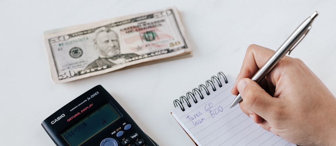 Person writing their budget and using a calculator.