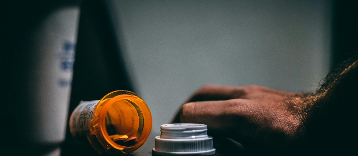 Person's hand near a spilled bottle of pills.