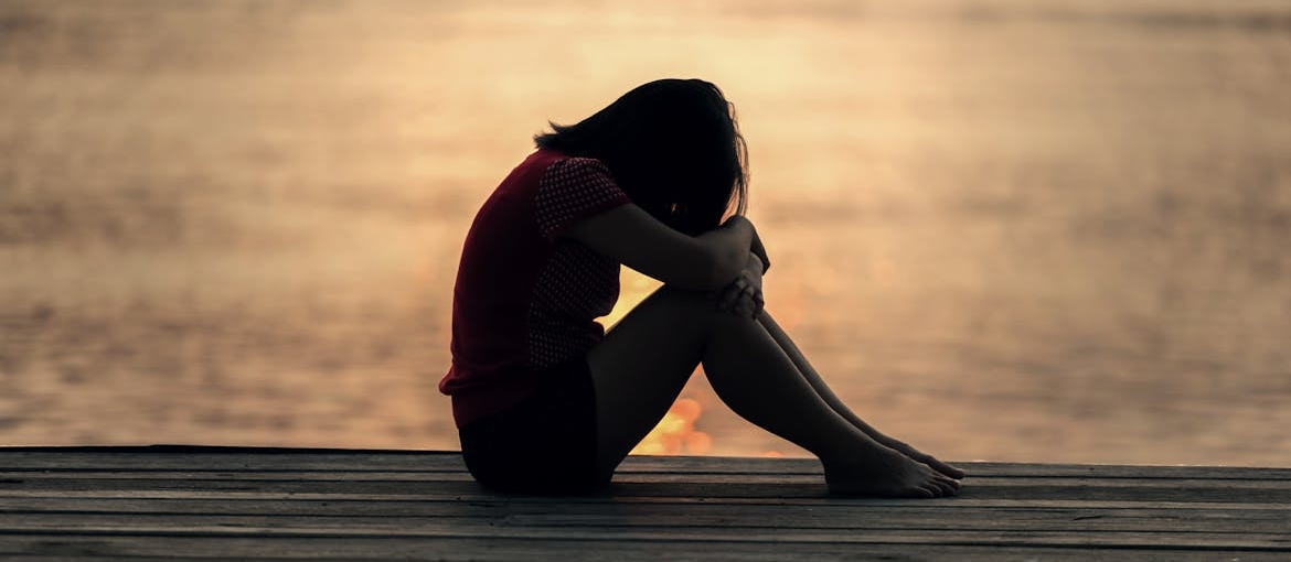 Woman sitting on the dock and hugging her knees.