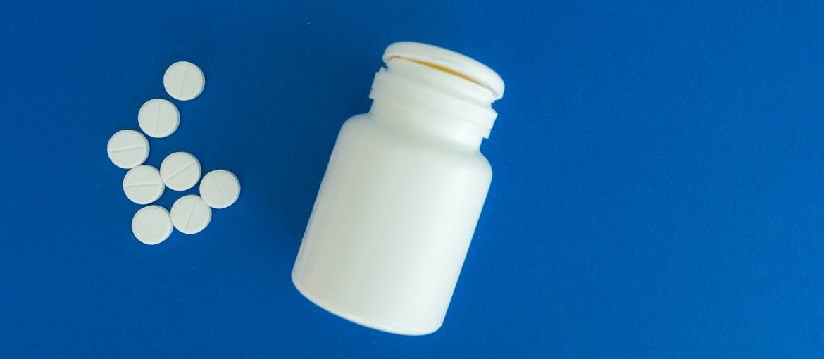 A white pill bottle with several round white pills scattered on a blue surface