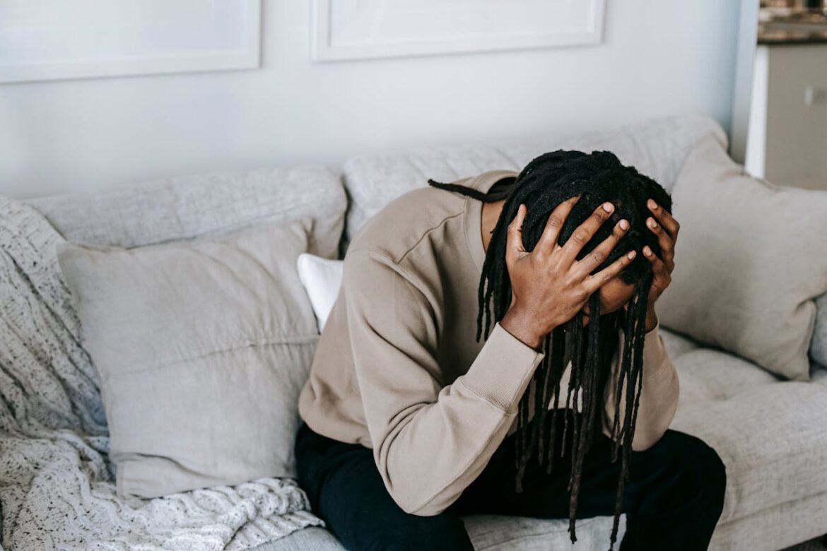 Man sitting on the couch and holding his head.