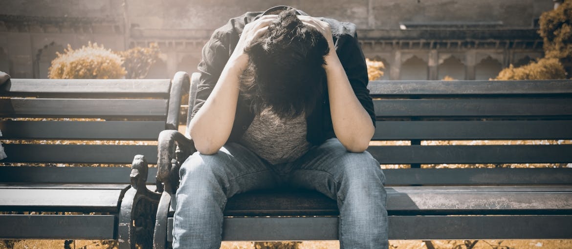Man sitting on a bench and holding his head.