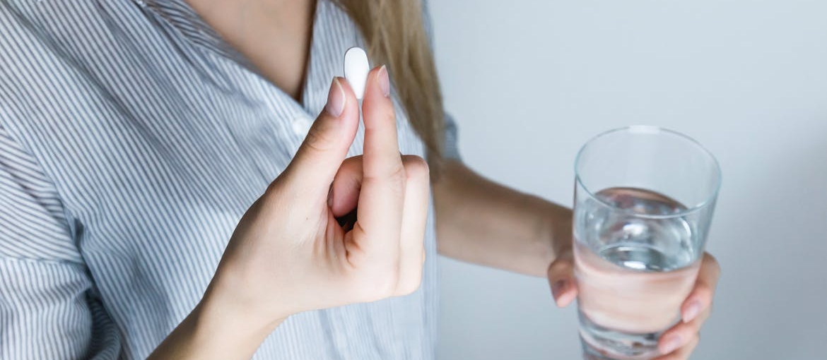 Woman holding a glass of water and a pill.