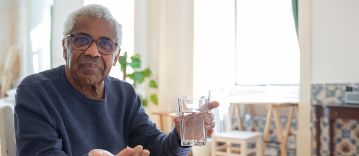 Older man holding a glass of water and pills.