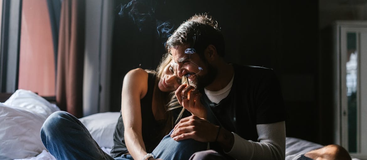 Two people smoking marijuana while sitting on a bed.