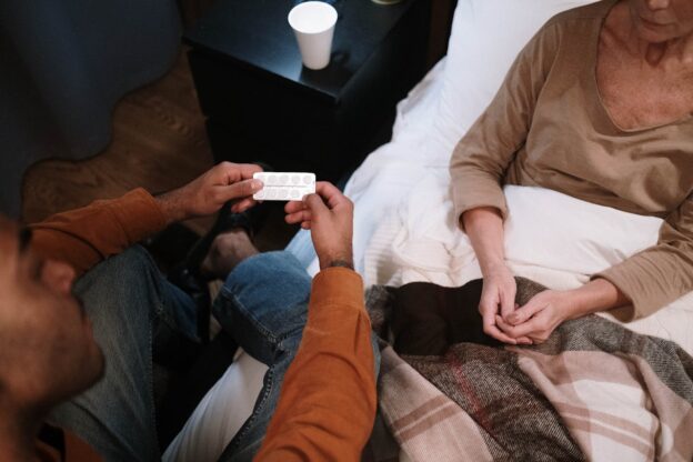 Man giving pills to an older woman.