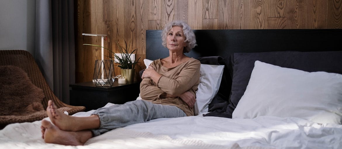 Older woman sitting on her bed alone.