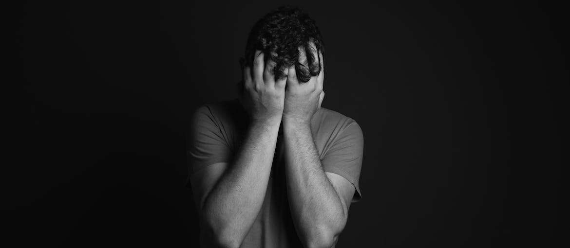 Man covering his face while struggling with dual diagnosis recovery challenges.