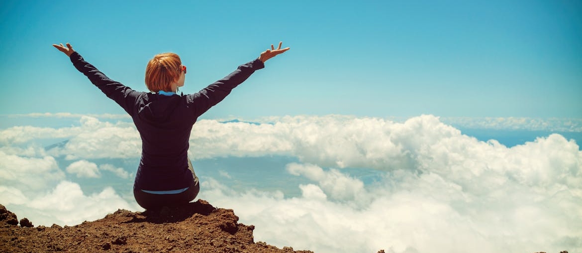 Woman sitting on the cliff and lifting her arms.