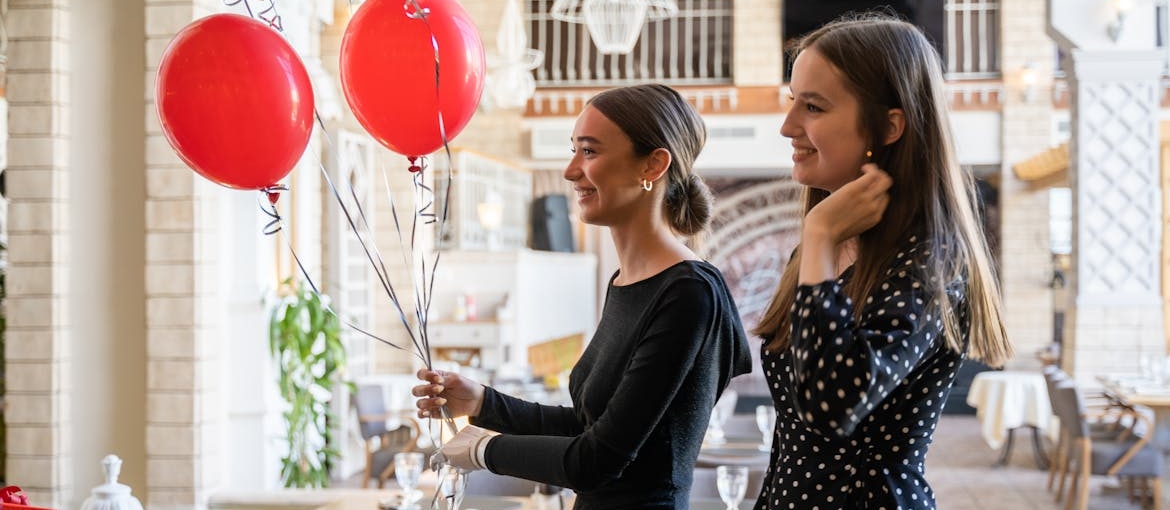 Two women attending a birthday party and holding balloons.