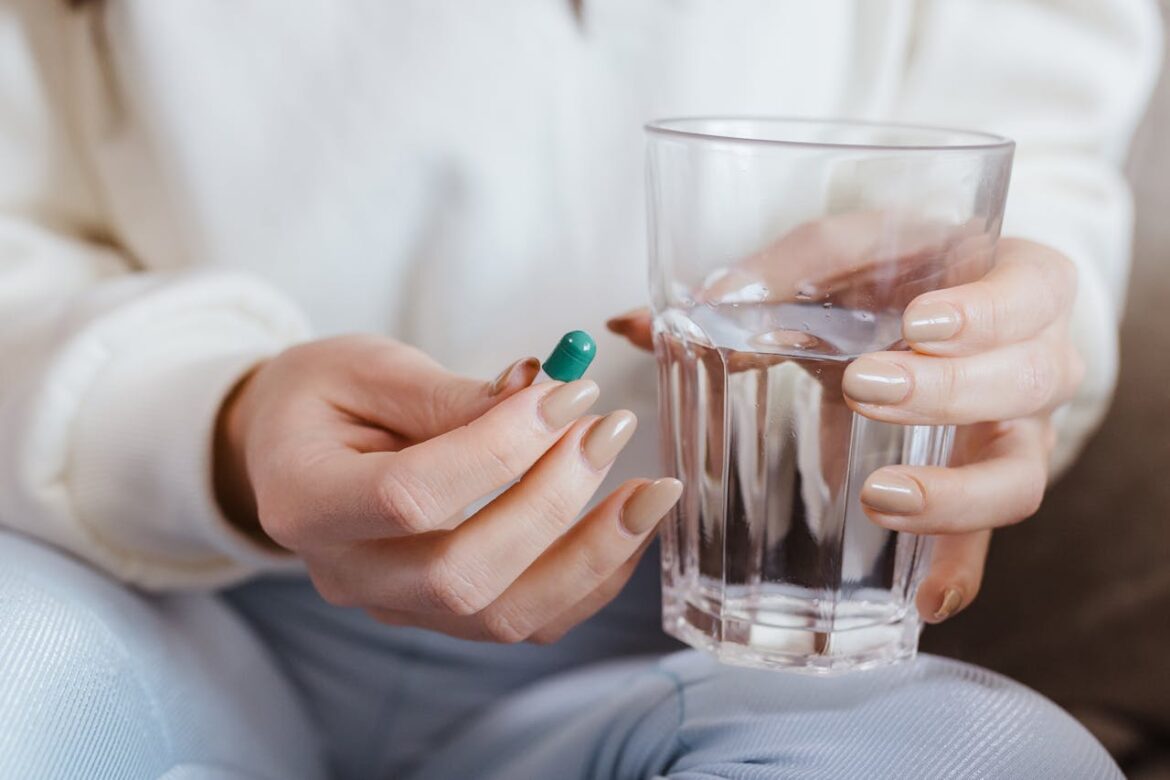 Person holding a pill and a glass of water.