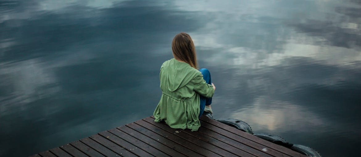 Woman sitting on the dock and looking at a lake.