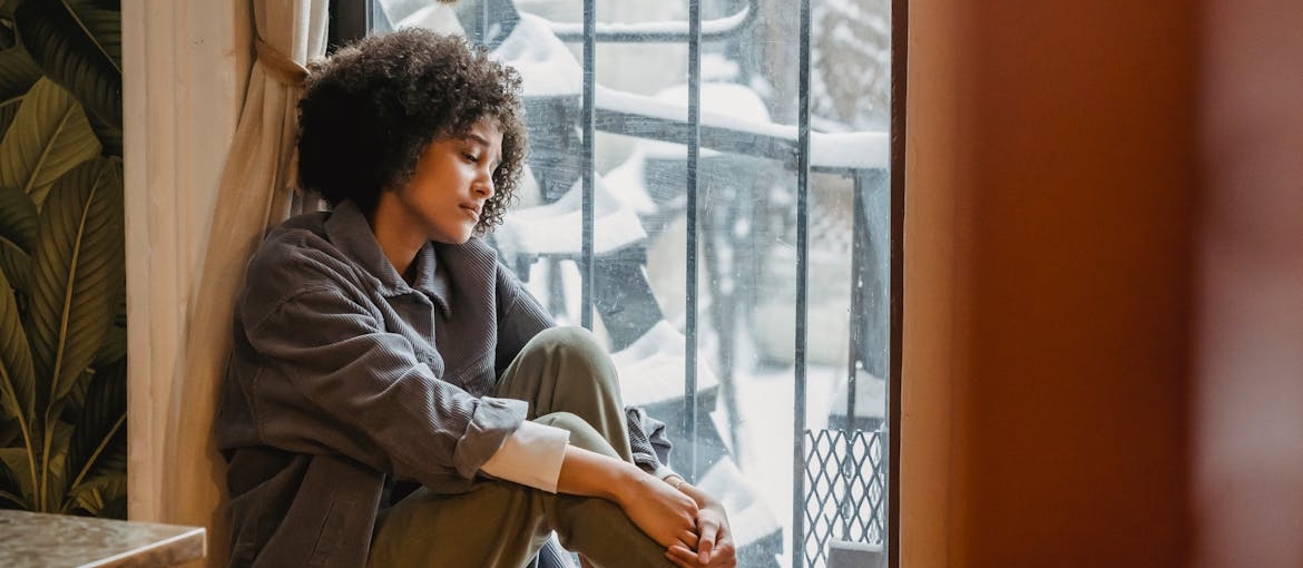 Woman experiencing seasonal depression looking out of the window.