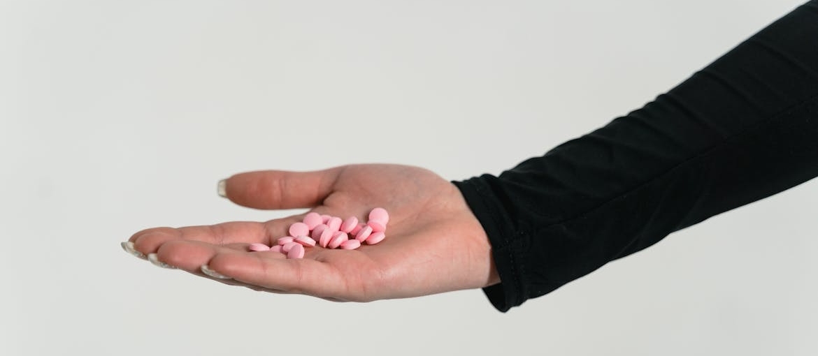 Person holding pink pills in their hand.