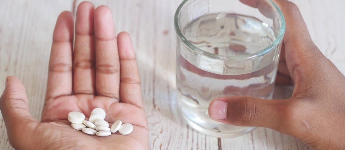 Person holding a glass of water and white pills.