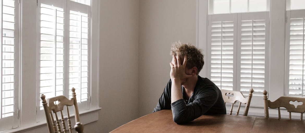 Stressed out man sitting at a kitchen table thinking about addiction and divorce.
