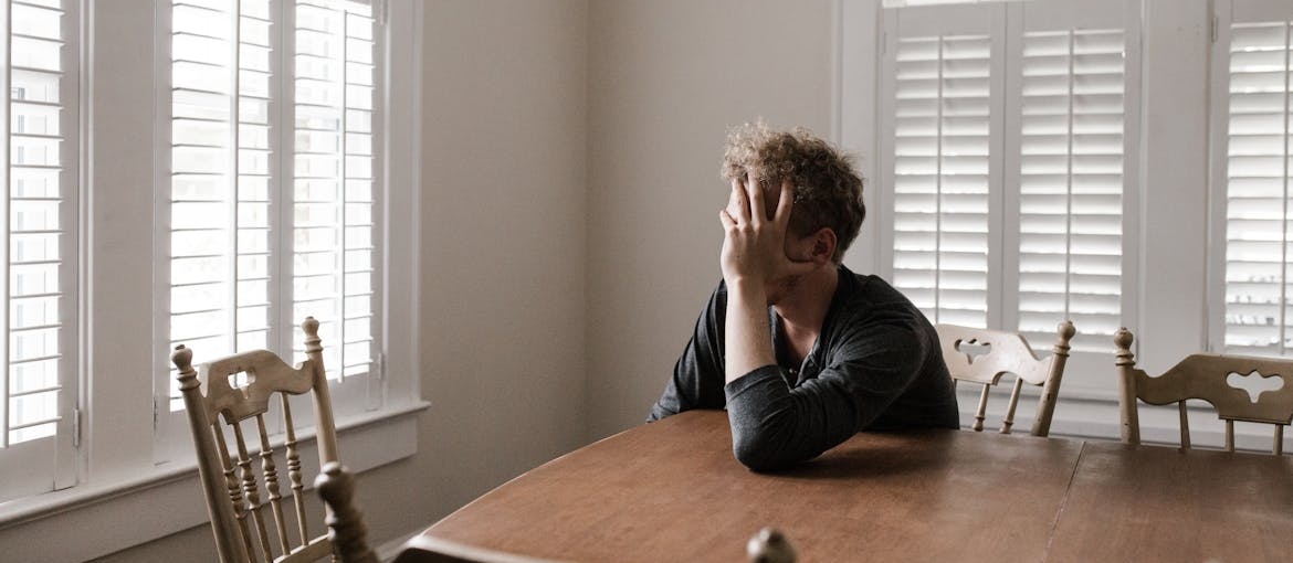 Sad man sitting at a table and thinking about coping skills for addiction.