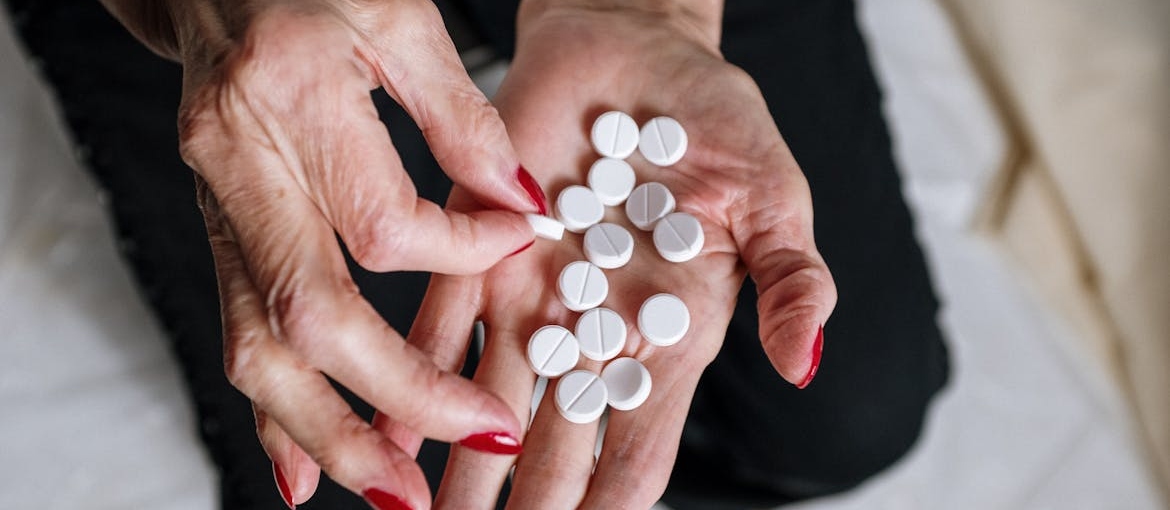 Elderly woman counting white pills on her hand.