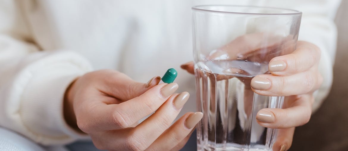 Person holding a pill and a glass of water.