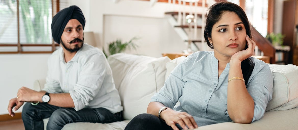 Husband and wife sitting on the couch after having a fight.