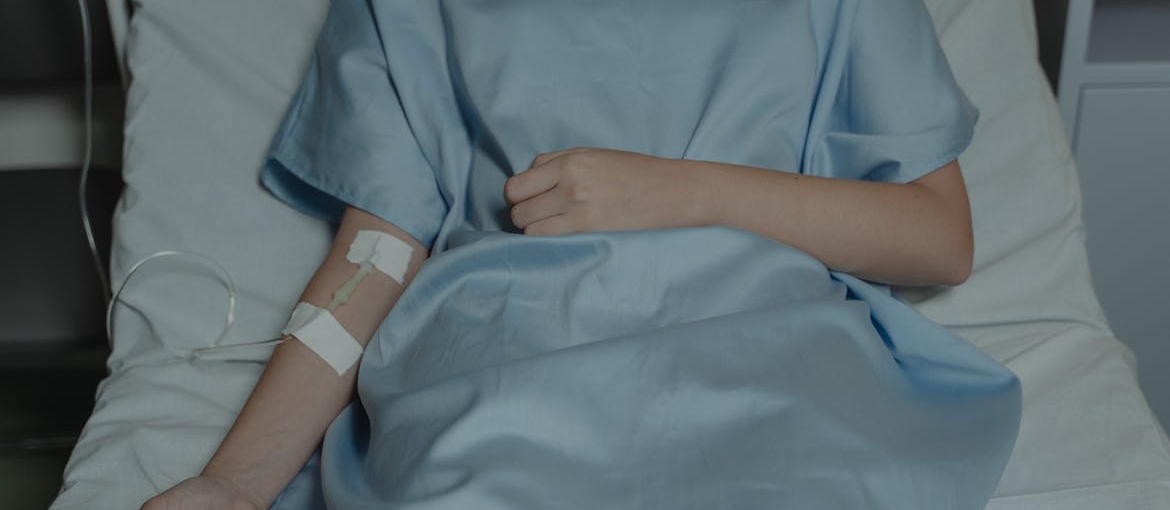 Person lying in a hospital bed with an IV in their arm.