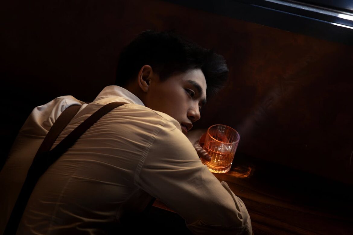 Man lying next to a glass of alcohol after experiencing an alcoholic relapse after long term sobriety.