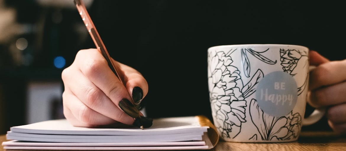 Woman writing in a notebook and drinking coffee.