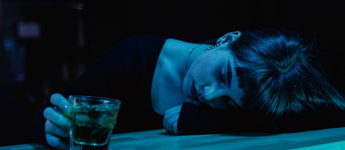 Woman leaning on a bar while drinking whiskey.