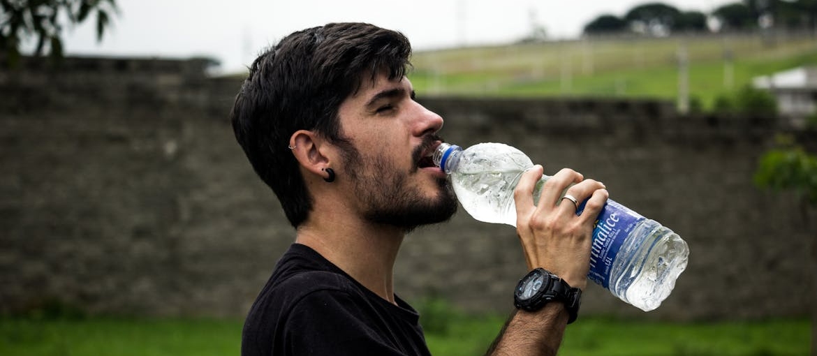 Man drinking water from a water bottle during a walk.