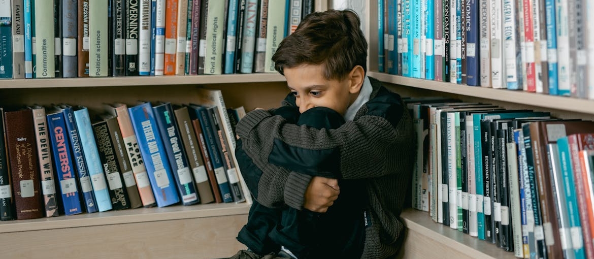Scared child of addicted parents sitting on the floor of a library.