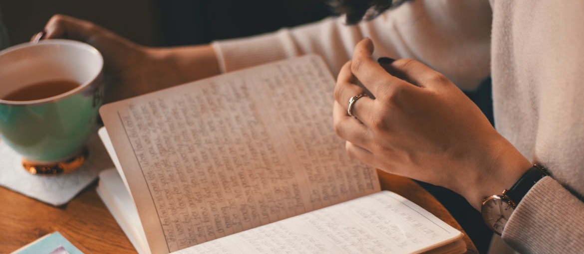 Woman drinking a cup of coffee and journaling.