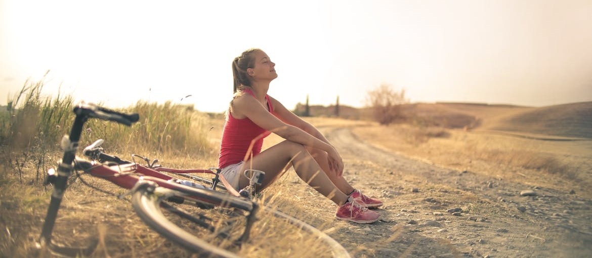 Woman sitting on the ground next to a bicycle and enjoying the sun.