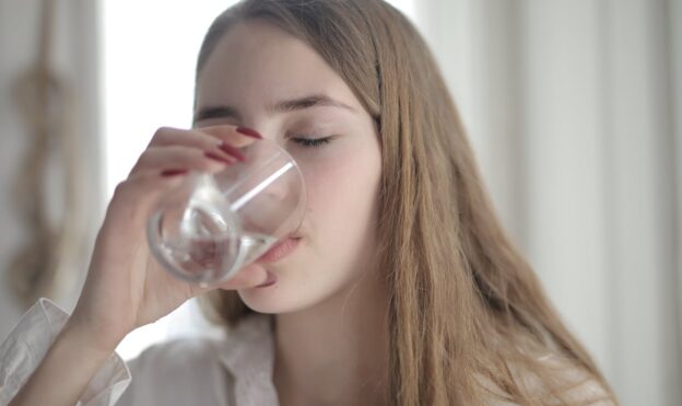 Woman drinking a glass of water after learning how to get weed out of your system.