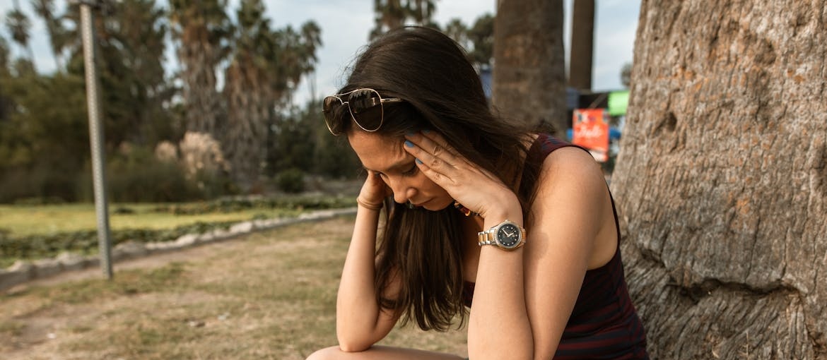 Stressed out woman crouching beside a tree.