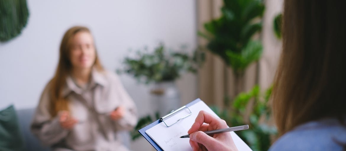 Woman writing in a clipboard while talking to a patient.