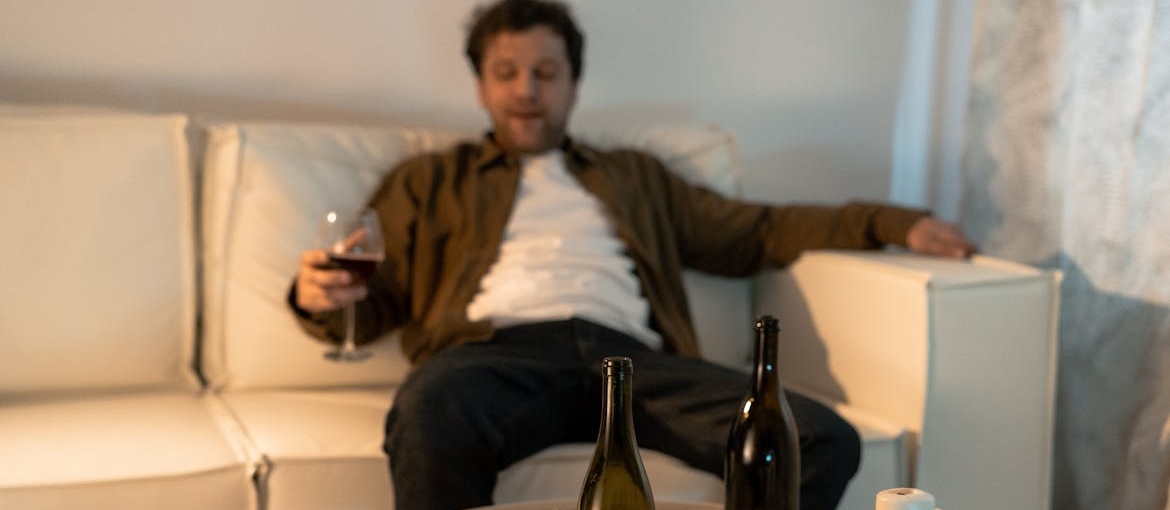 Man drinking a glass of wine while struggling with alcohol abuse and poverty.