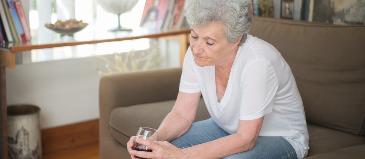 Woman sitting on the couch drinking a glass of wine while struggling with grief and substance abuse.