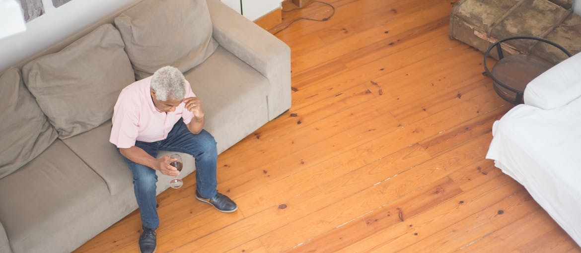 Man sitting on the couch drinking a glass of wine while struggling with grief and substance abuse.