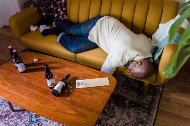 Man sleeping on the couch while struggling with alcohol abuse and poverty.