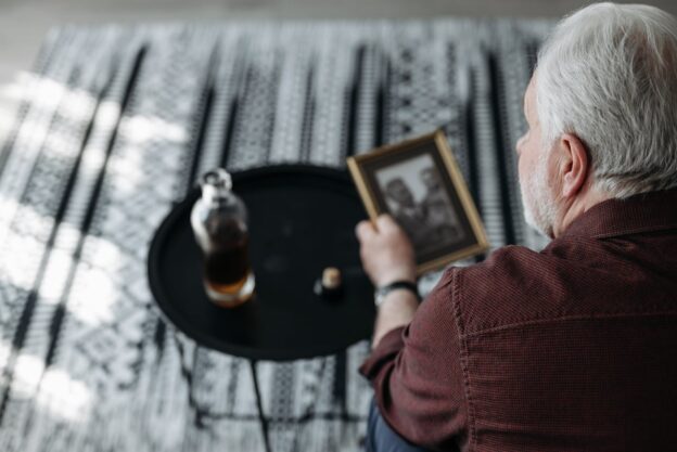 Man sitting on the couch drinking a glass of wine while struggling with grief and substance abuse.