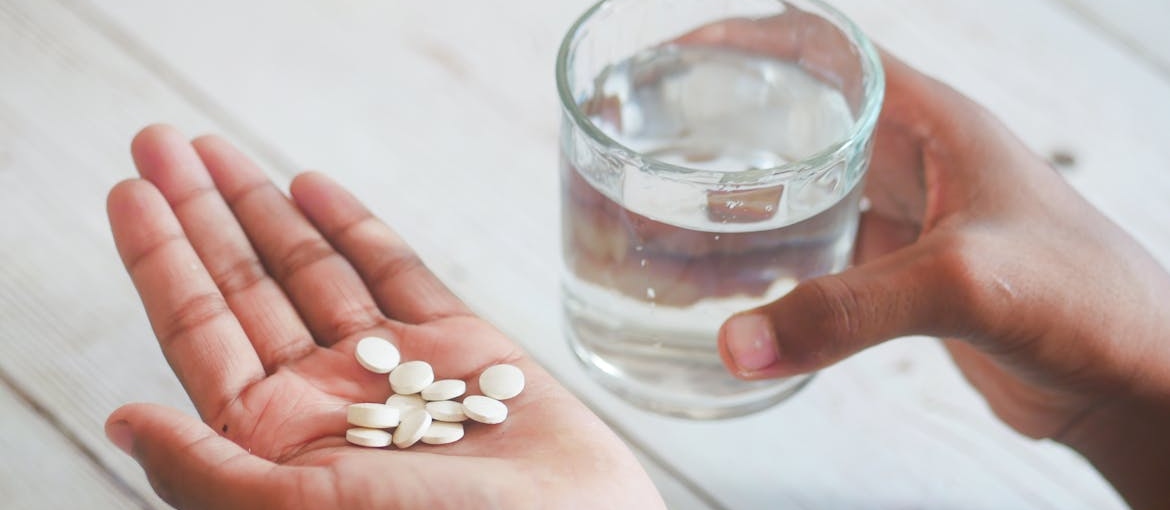 Person holding a glass of water and a bunch of pills.