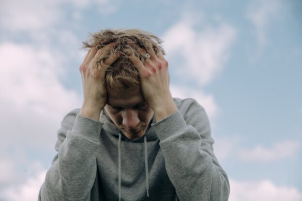 Man holding his head and experiencing how drugs influence a person's emotions perceptions and behavior.