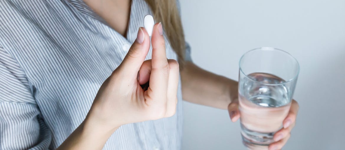 Woman holding a pill and a glass of water.