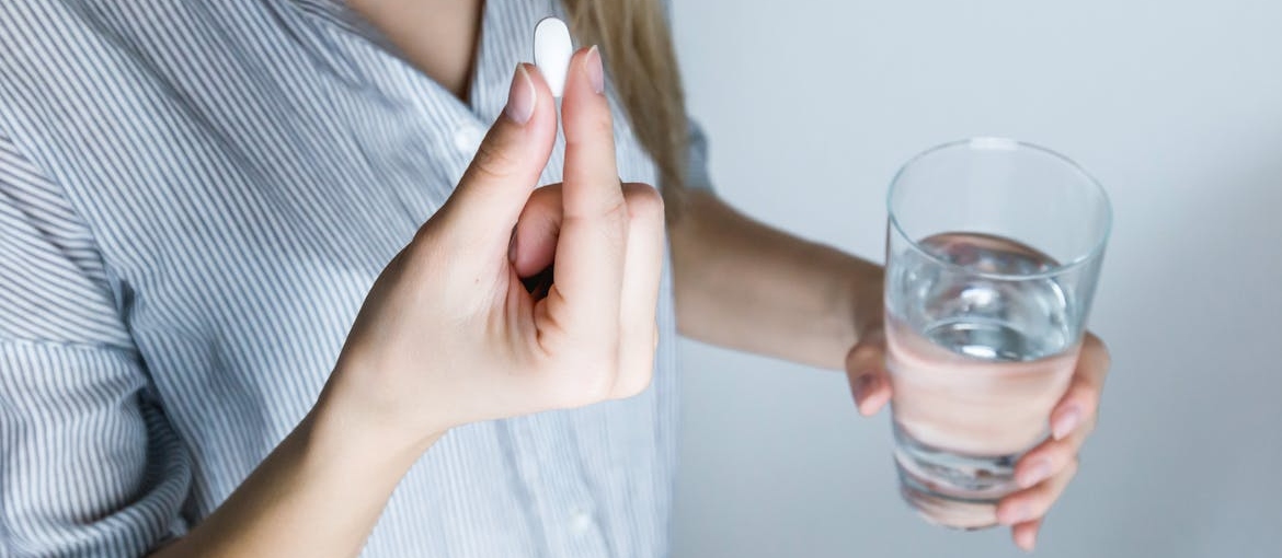 Woman holding a pill and a glass of water.