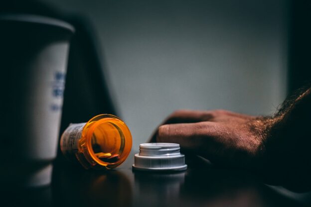 Man's hand next to an open bottle of pills.