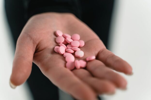 Woman holding a bunch of tiny pink pills.