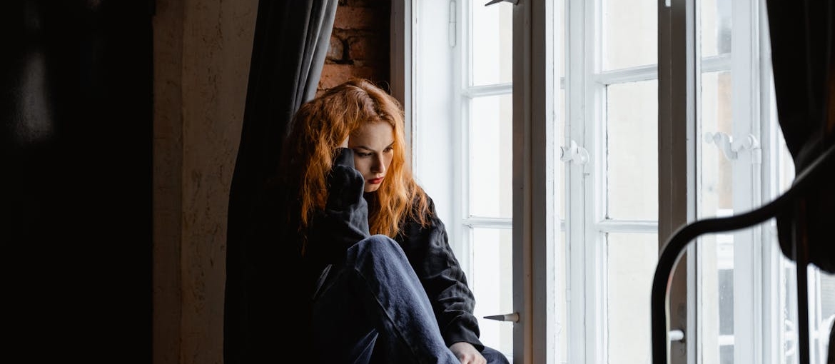 Worried woman sitting near a window and looking outside.